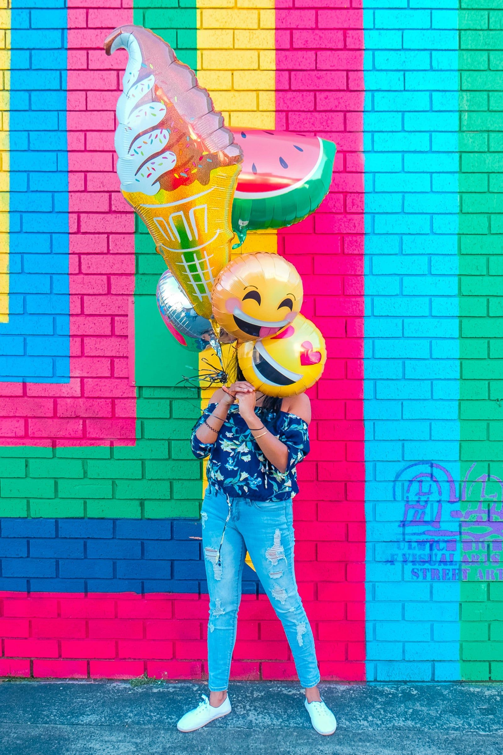 Person holding emoji balloons in front of a brightly painted wall