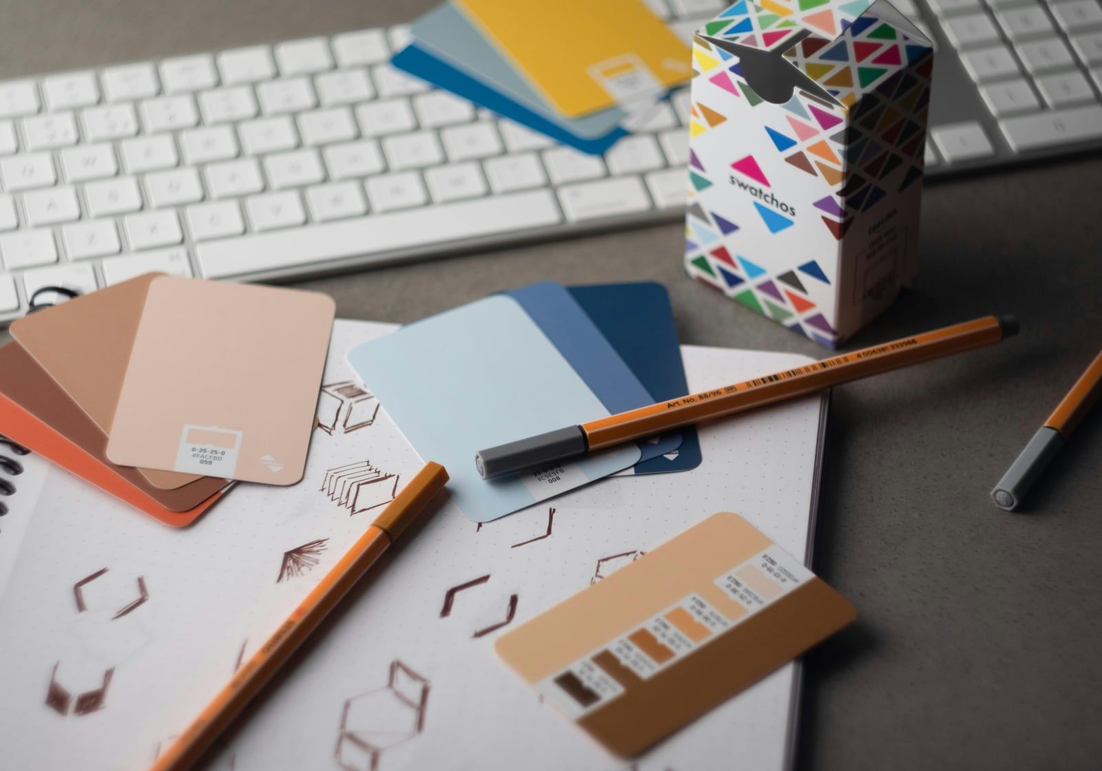 Colour swatches, pens and logo sketches on a desk beside a keyboard