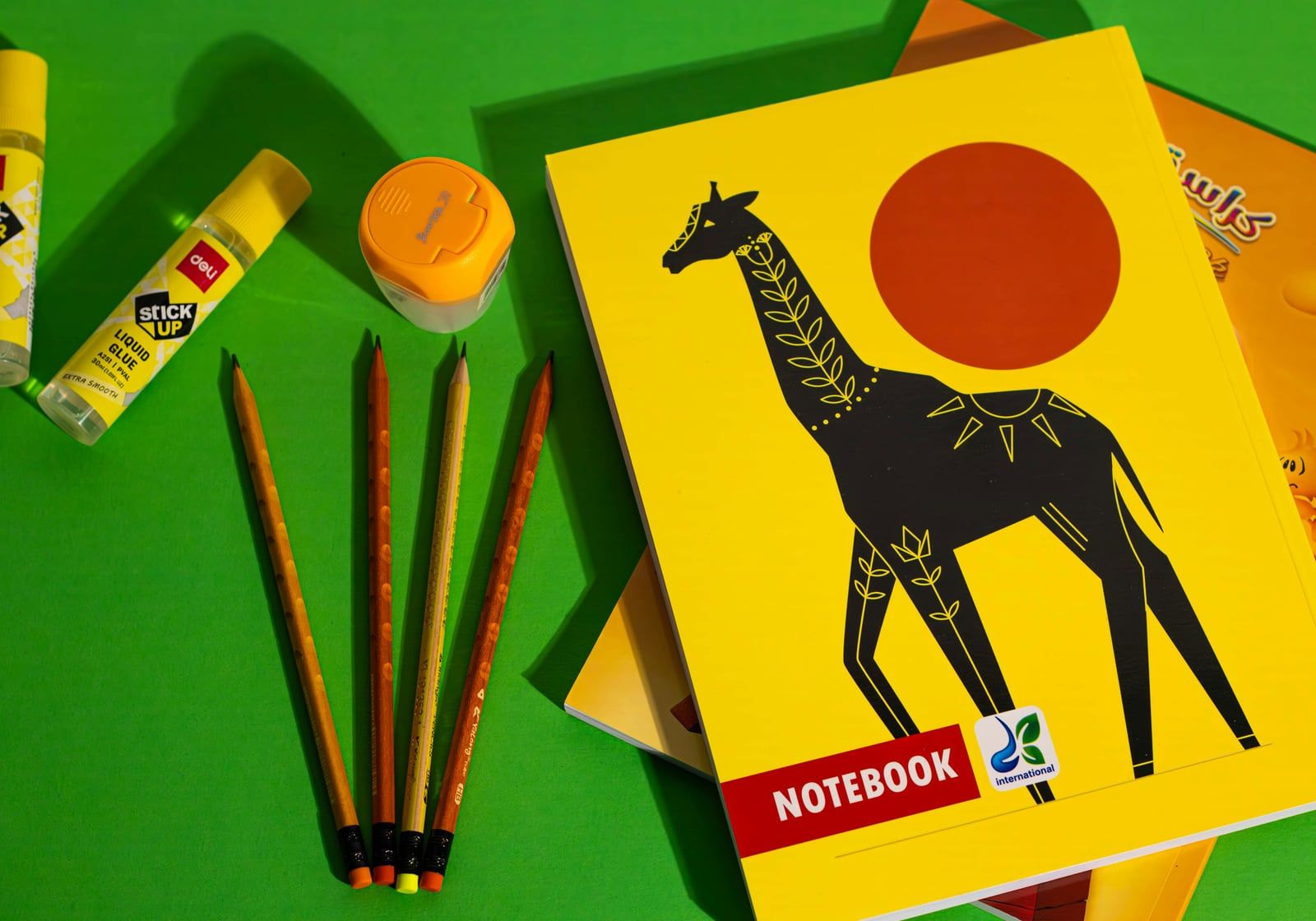 Notebook with a giraffe cover beside pencils, glue and a sharpener