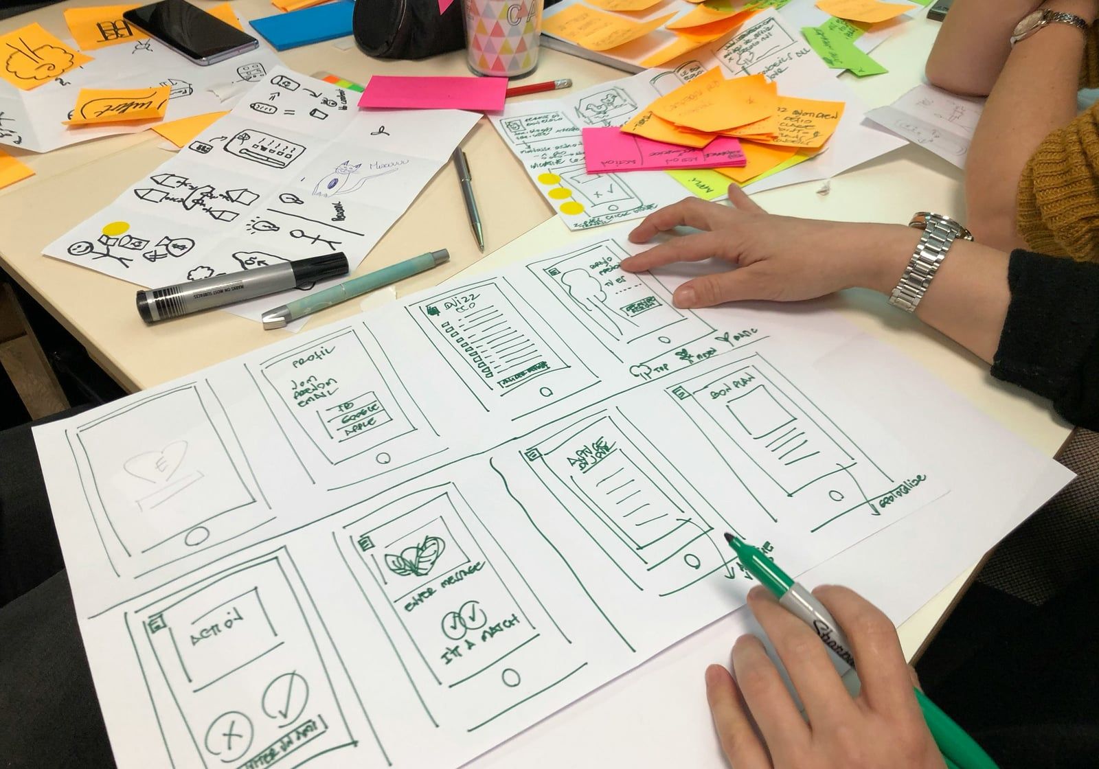 Hand-drawn mobile app wireframes surrounded by sticky notes and pens